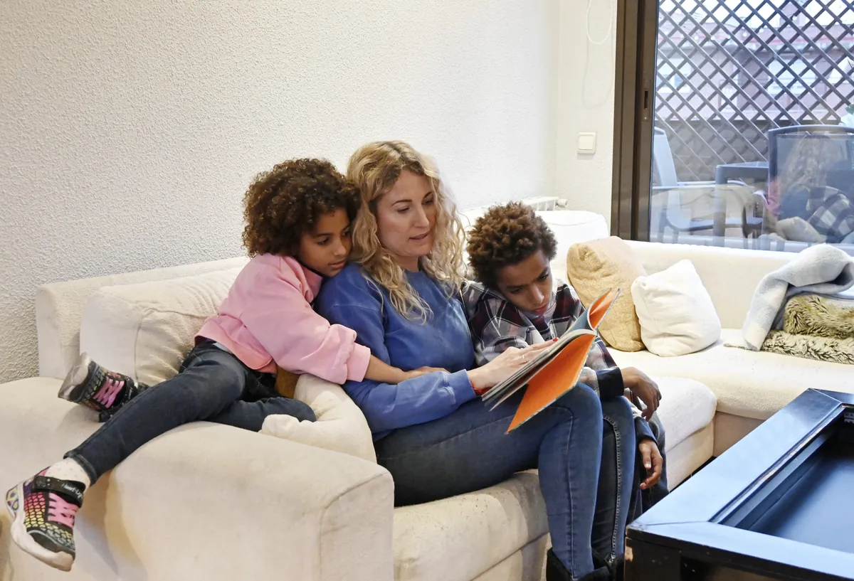 A parent reading a book with her two children at home — the everyday reality of a homeschool social studies lesson.
